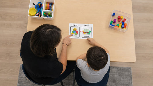 ABA therapist using a First-Then visual board with a young boy during a therapy session, showing "Blocks" first and "Reading" next to support task completion and transitions.